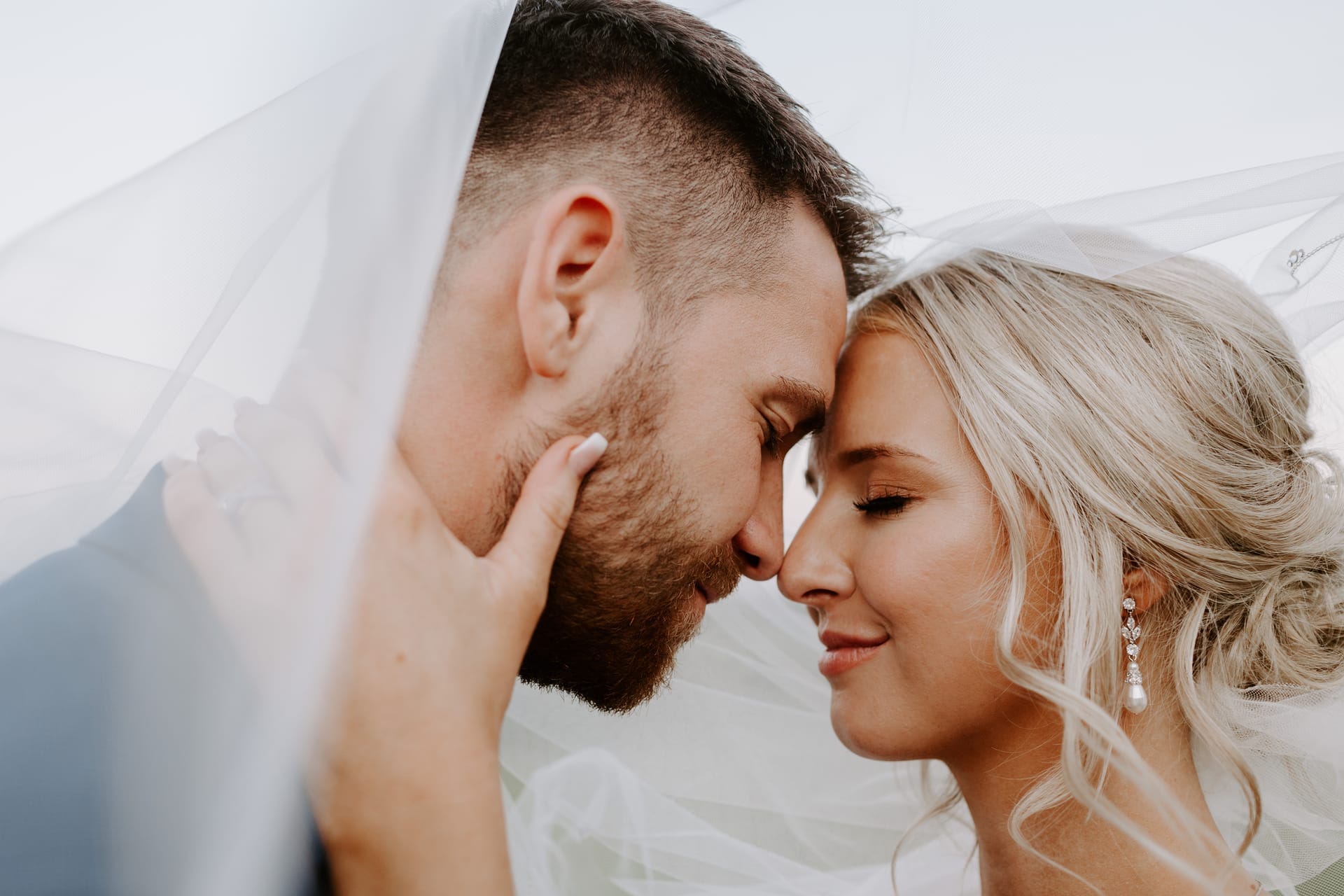 Groom and bride touching foreheads beneath her veil