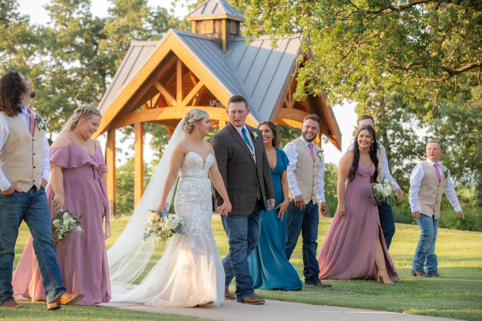 Bride and groom walking with their wedding party past a timber pavilion