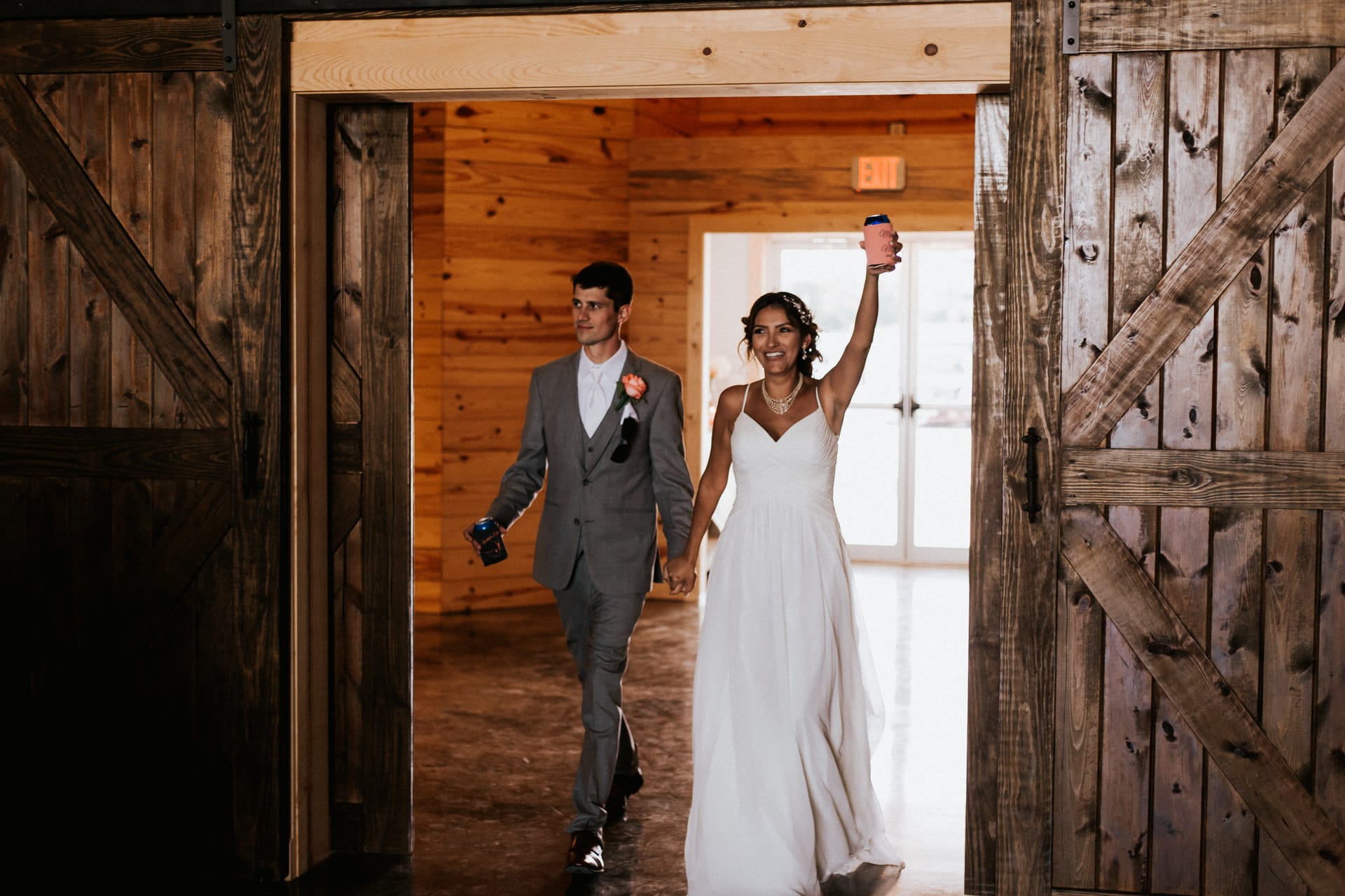 Bride and groom entering through open wooden barn doors, bride with her arm raised