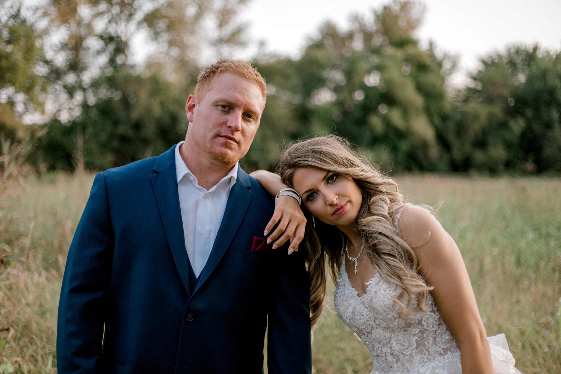 Bride leaning on the groom's shoulder in a grassy field